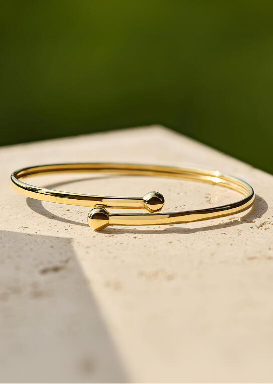 An overlapping bangle bracelet with beaded ends crafted in 14k yellow gold. 