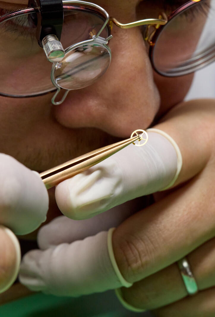 A watchmaker carefully examines the parts of a luxury watch through a loupe.