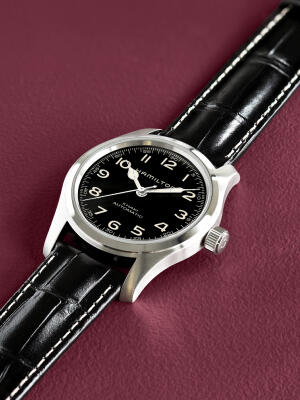 Hamilton field watch with a black dial rests on a purple surface