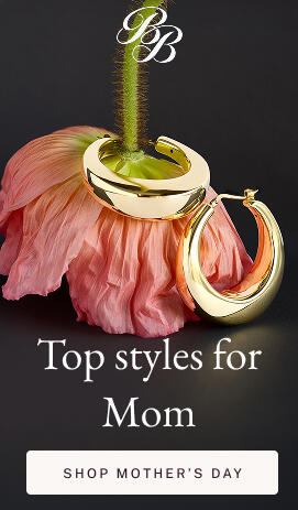 A fluted yellow gold hoop encircles the stem of an upside down pink flower on a dark gray surface.