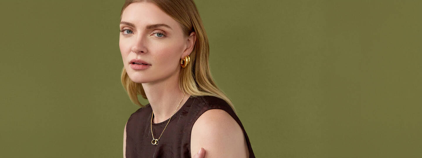 A woman wearing gold hoop earrings and necklace with interlocking circles.
