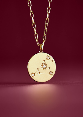 Yellow gold necklace with a zodiac pendant shines against a purple backdrop.