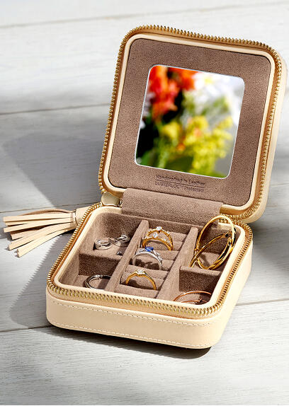 A travel sized jewelry box with gemstone rings and hoop earrings inside.