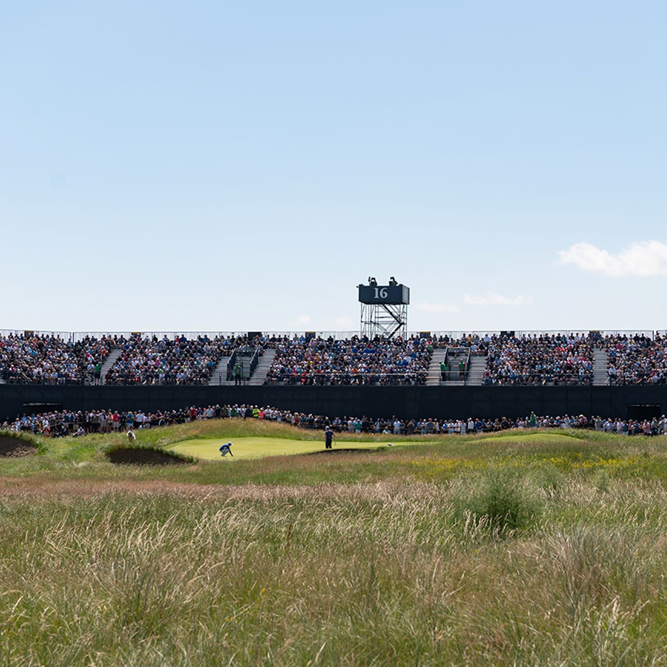 The stands packed with fans as golfers putt at The Open golf tournament