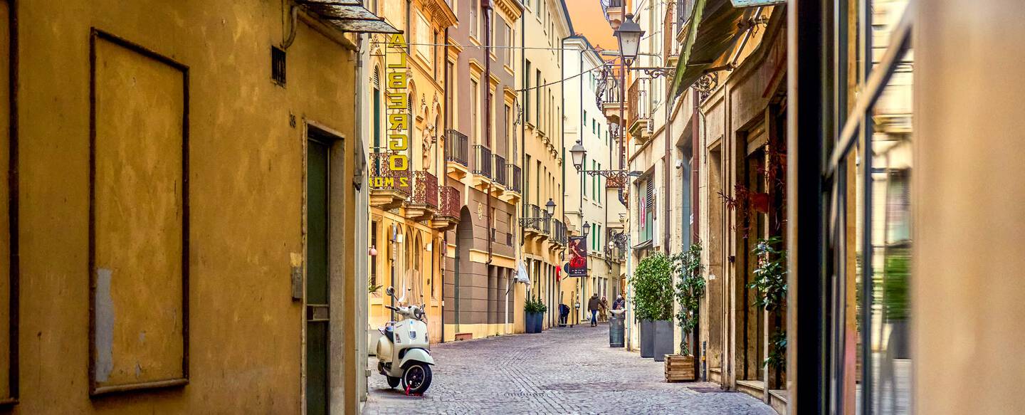 A narrow cobblestone street winds through a residential area in an Italian city.