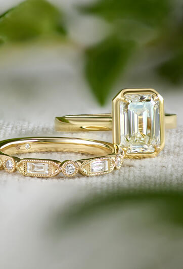 A diamond bridal set rests atop a fabric surface with out of focus greenery in the background.