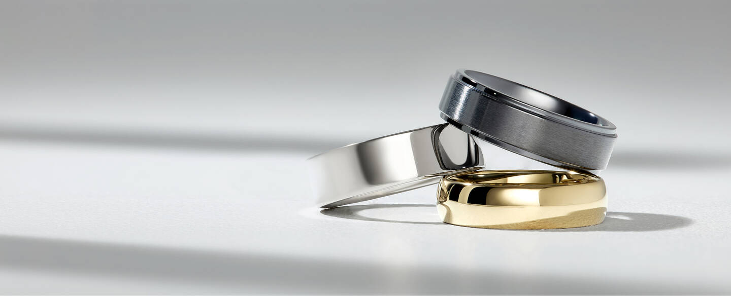 A stack of custom men&rsquo;s wedding bands in a variety of precious metals and customization options.
