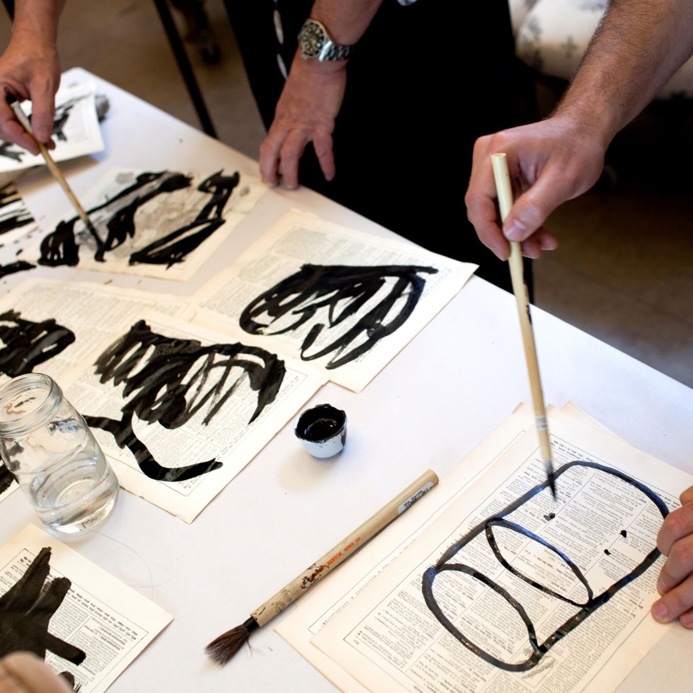 artists hands are holding paintbrushes and painting on printed paper with lettering