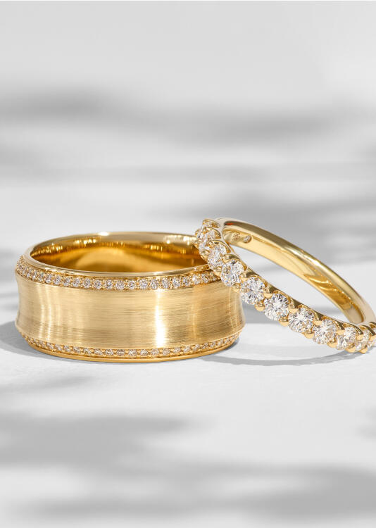 A yellow gold band in a satin finish features a perimeter of round diamonds while a diamond anniversary ring sparkles alongside it.