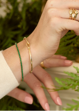 Closeup of a woman's wrist wearing one gold and one gemstone bracelet. 