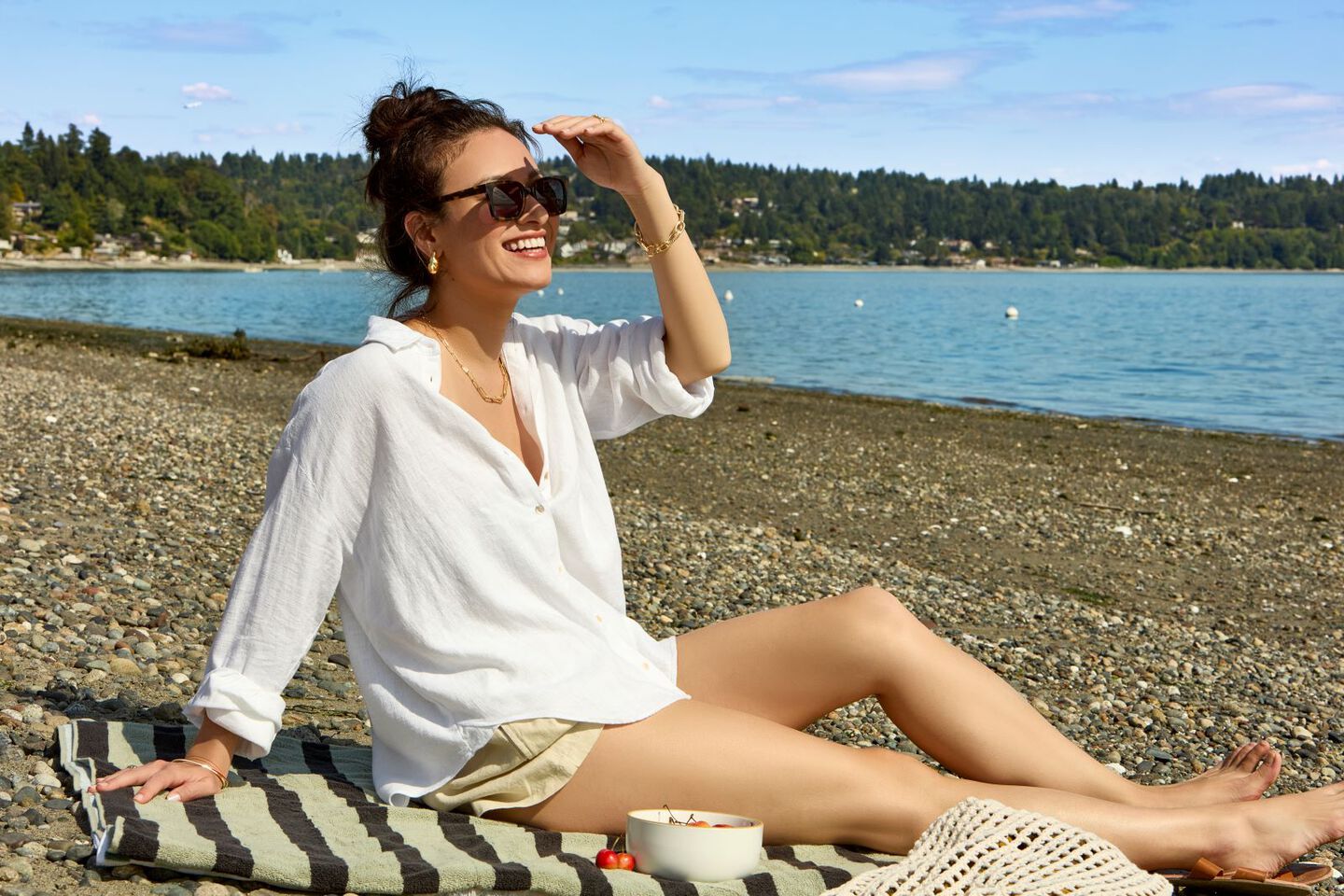 woman in white shirt sitting on the beach, using her hand to shade the sun from her eyes