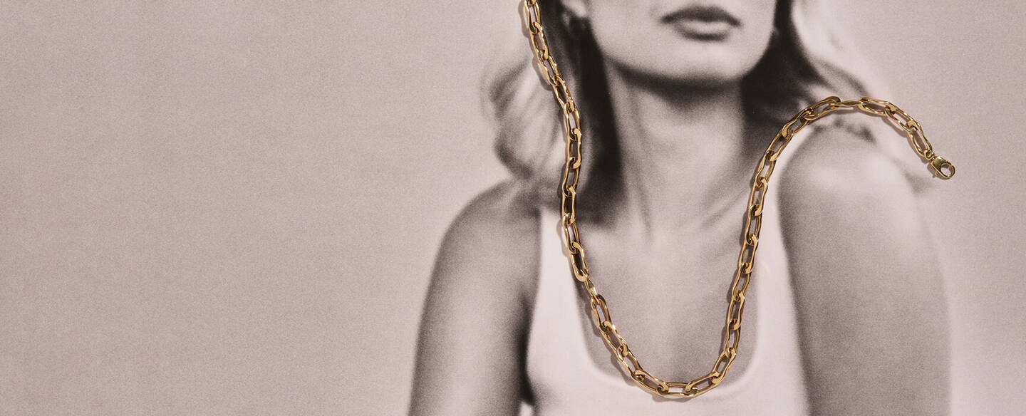 Black and white photo of a woman gazing peacefully toward the horizon. The only item in color is an Italian-made yellow gold necklace.