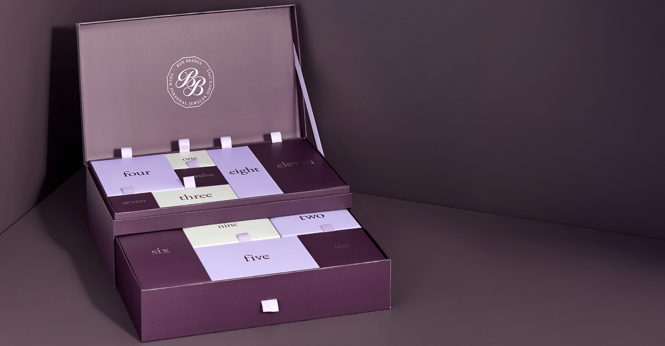 The 2025 Ben Bridge Advent Calendar opens to reveal twelve individually boxed gifts in varying shades of purple.