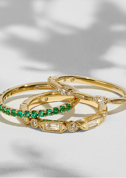 A stack of anniversary bands featuring diamonds and colored gemstones set in 14k yellow gold.