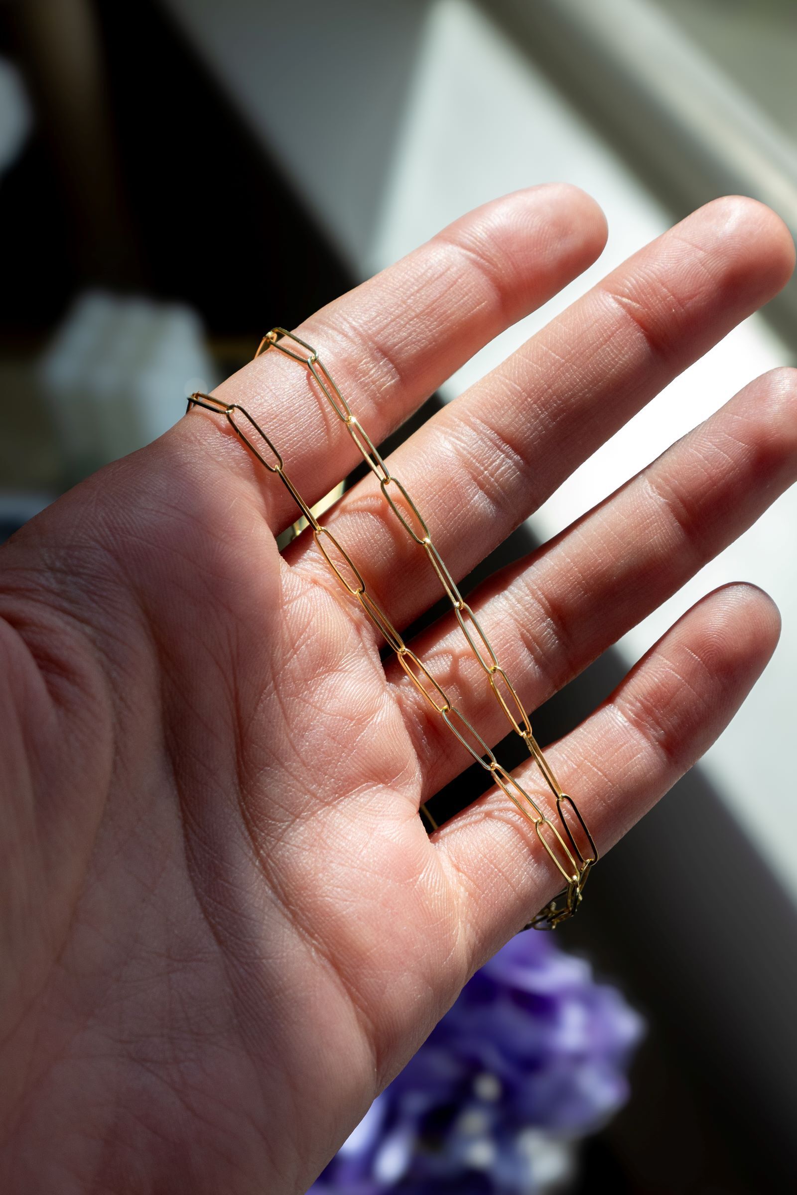 A yellow gold paperclip chain is draped across a woman's fingers A yellow gold paperclip chain is draped across a woman's fingers