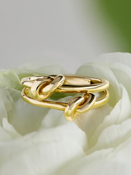 A yellow gold ring with knots of gold rests atop white flower petals. 