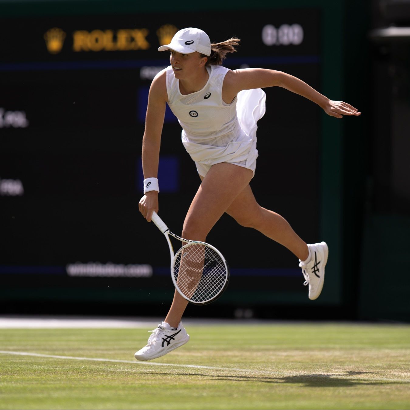 Professional tennis player in a white dress returns a volley at Wimbledon