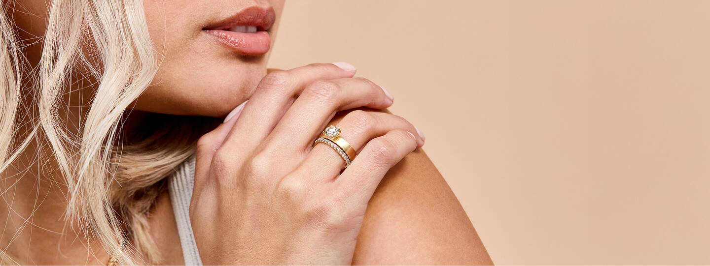 A woman wearing a yellow gold engagement ring and diamond wedding band gazes over her shoulder. 