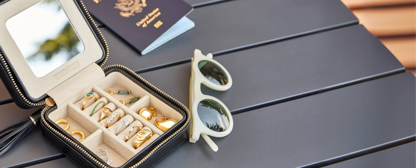A travel jewelry case with fine jewelry, sunglasses and passport are spread out on a table top.
