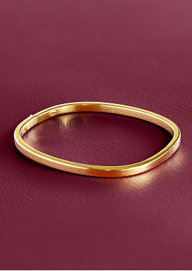 A yellow gold bangle rests on a smooth purple surface