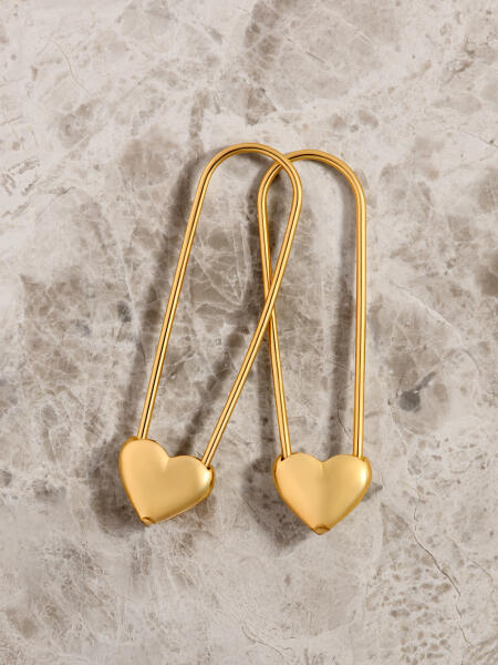 Paperclip style yellow gold earrings with heart-shaped clasps on a marble surface