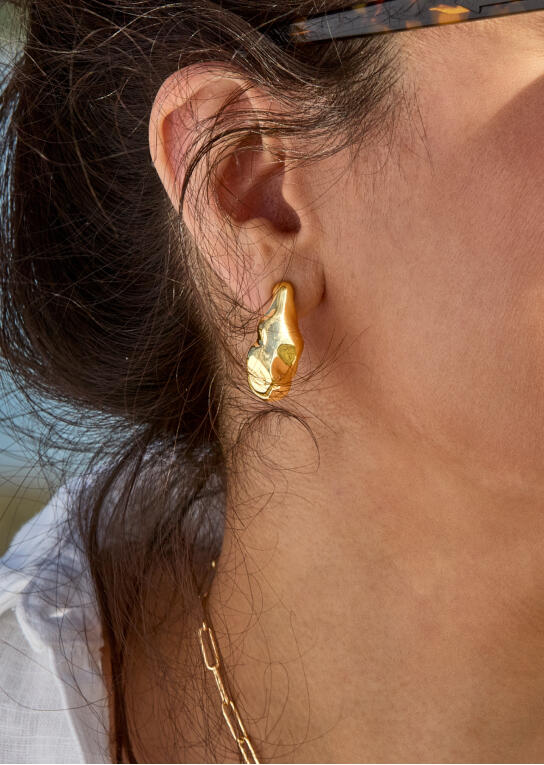 A woman&rsquo;s ear with a bold yellow gold hoop earring