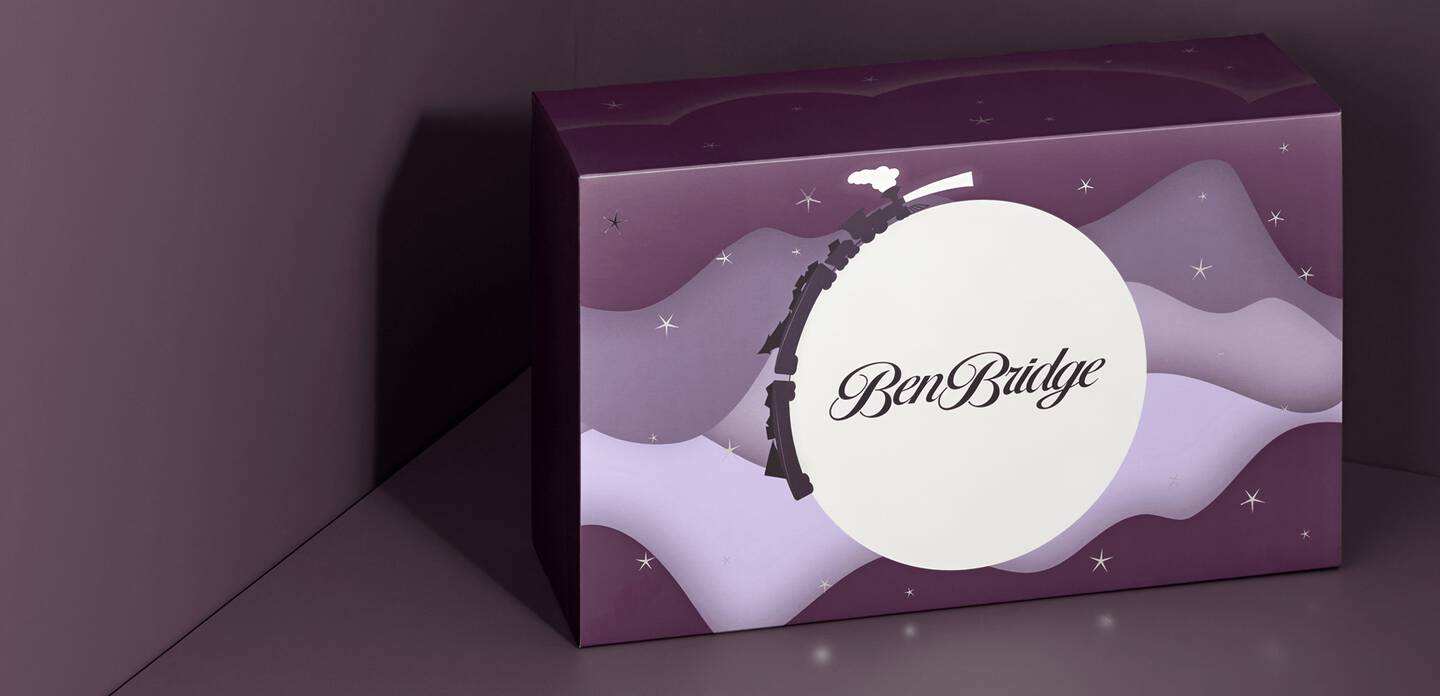 The Ben Bridge advent calendar, unopened, depicts a night sky with a full moon and twinkling stars.old-colored bowtie sits atop a holiday gift box while a woman smiles before opening her gift. 