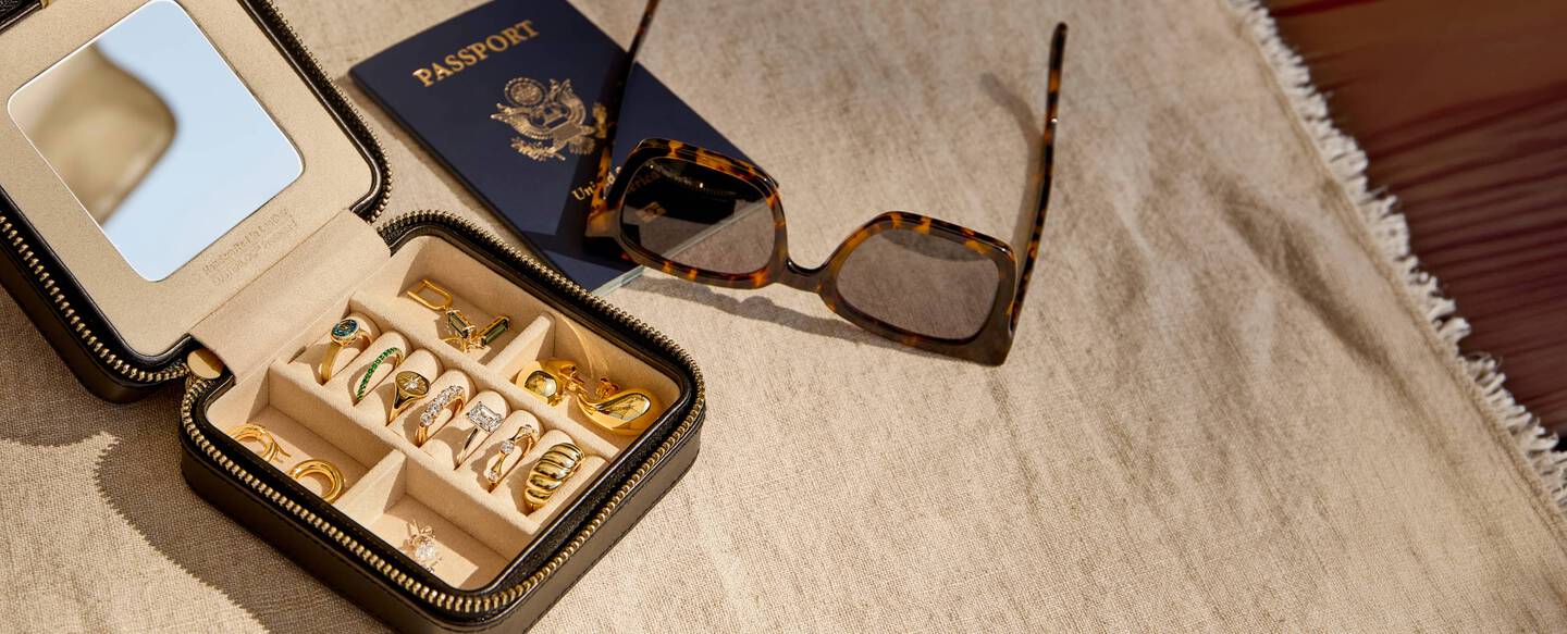 A passport, sunglasses and travel jewelry box with gold and gemstone jewelry inside