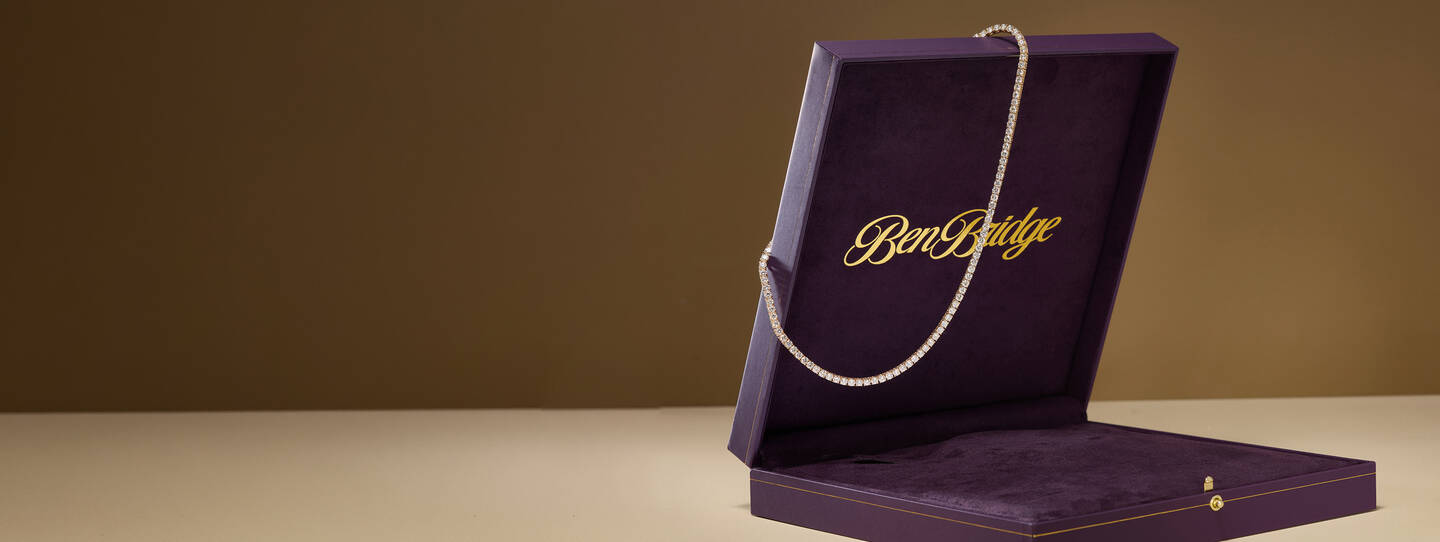 A diamond necklace hangs from the corner of a purple jewelry box with gold lettering.