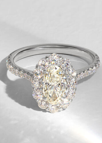 Pear shaped diamond halo engagement ring set in white gold with an off-white background.