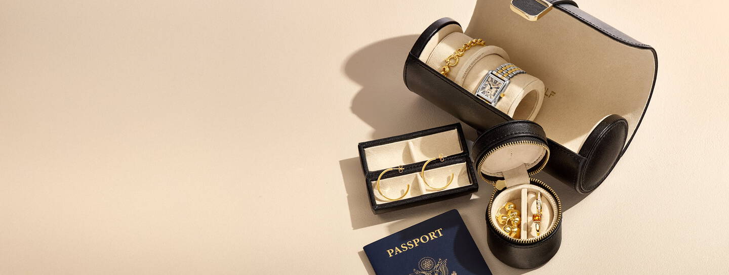 A passport and travel cases holding fine jewelry and watches cast shadows on a tan background.