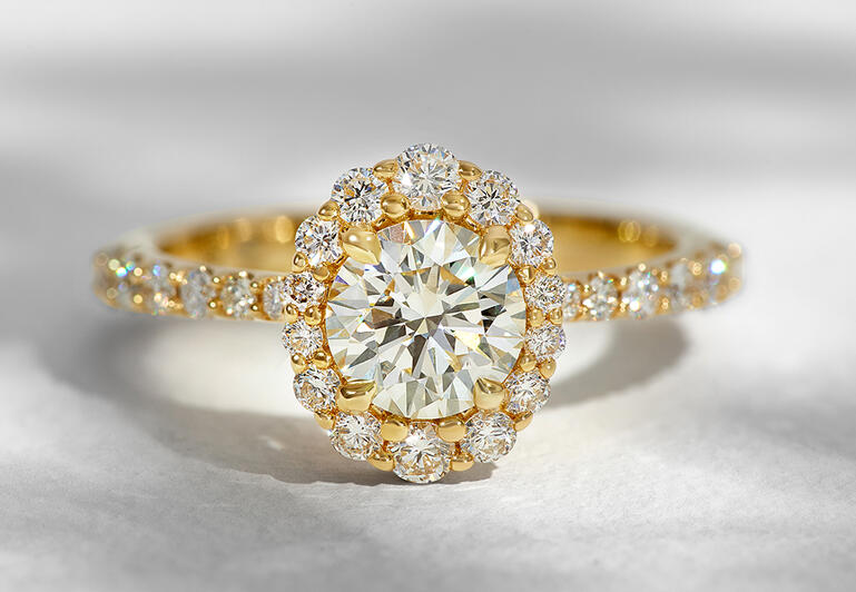 A diamond engagement ring in yellow gold featuring a halo of round diamonds and diamonds set along the shank. 