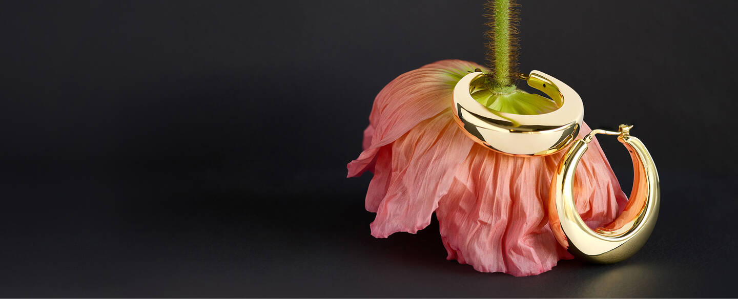 A gold hoop encircles the stem of an upside down flower on a dark gray surface. 