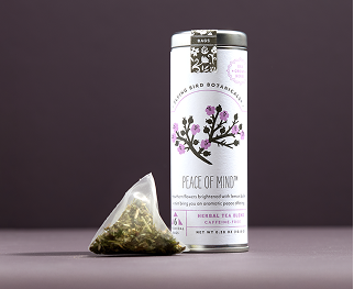A loose tea bag rests next to a packaging tube of Peace of Mind tea from Flying Bird Botanicals