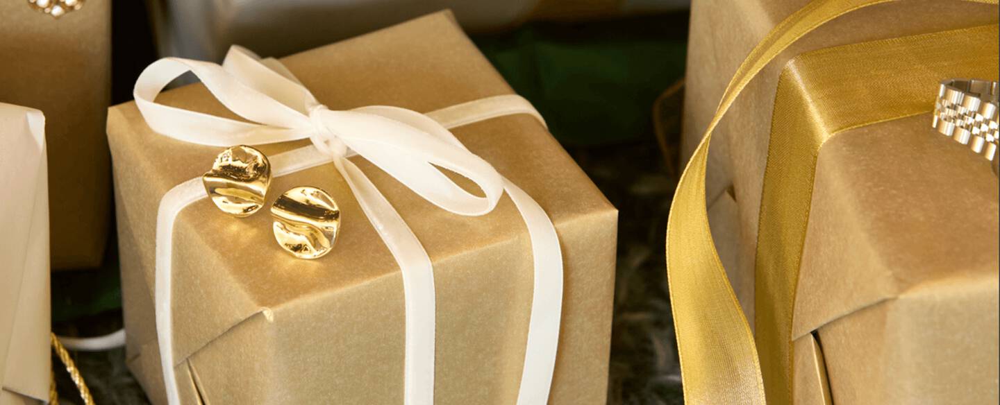 Gold studs rest atop a gift box adorned with a white ribbon.