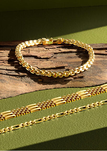 A yellow gold bracelet rests on a piece of driftwood above two yellow gold bracelets on a green surface.