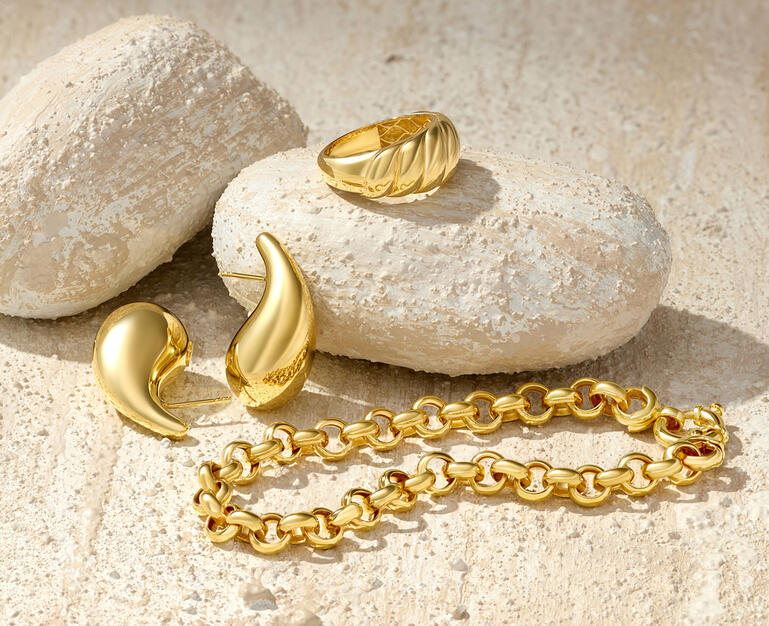 A yellow gold bracelet, gold teardrop earrings and a gold ring are shown amid a textured stone background. 