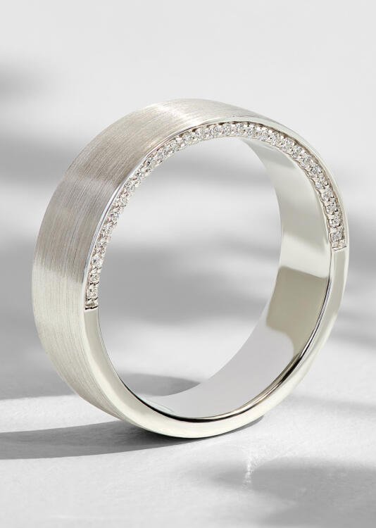 A matte finish white gold wedding band with natural round diamonds set along the wall of the band. 