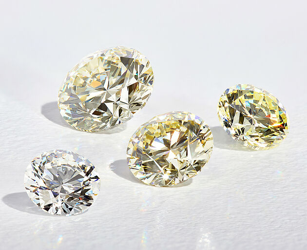 Loose diamonds in varying shades on a smooth white surface.