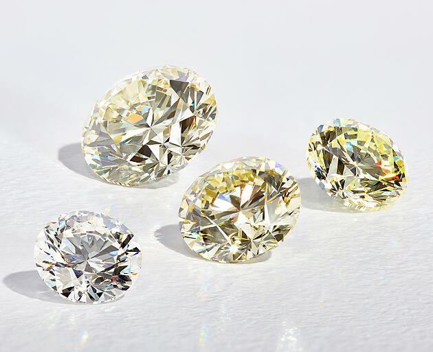 Loose diamonds in varying shades on a smooth white surface.