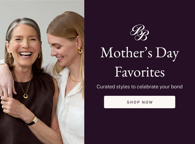 A mother embraces her daughter, both smiling and wearing yellow gold jewelry. 