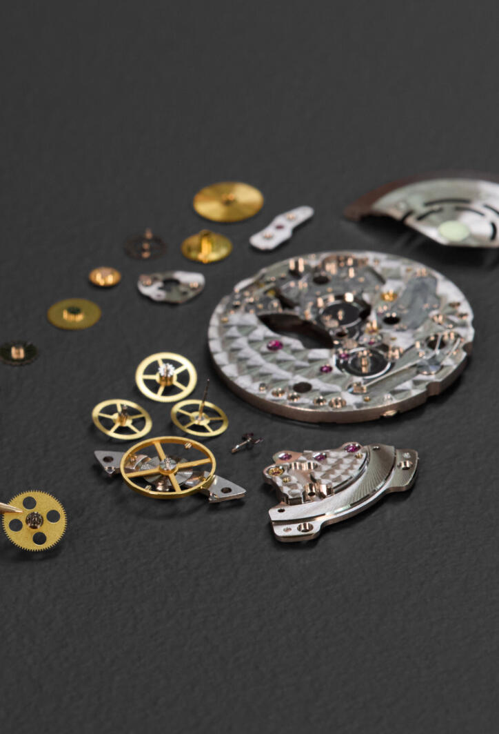 The parts of an automatic watch movement laid out on a dark gray surface.