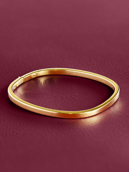 A yellow gold bangle on a smooth purple surface.
