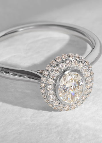 A round diamond double halo engagement ring set in white gold sparkles against an off-white background.