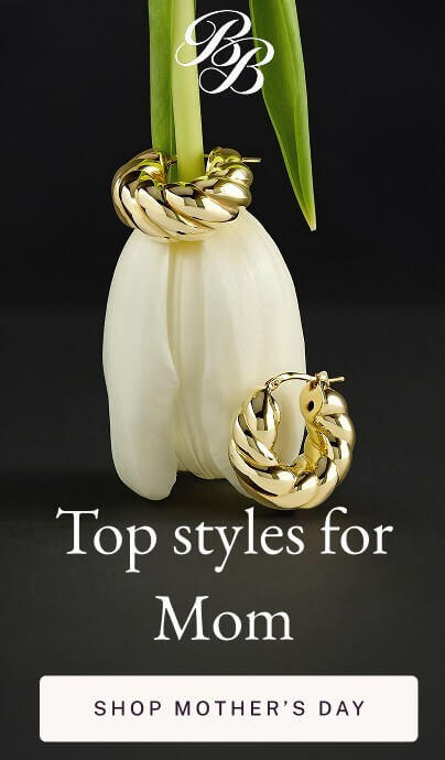 A gold hoop encircles the stem of an upside down white flower on a dark gray surface.