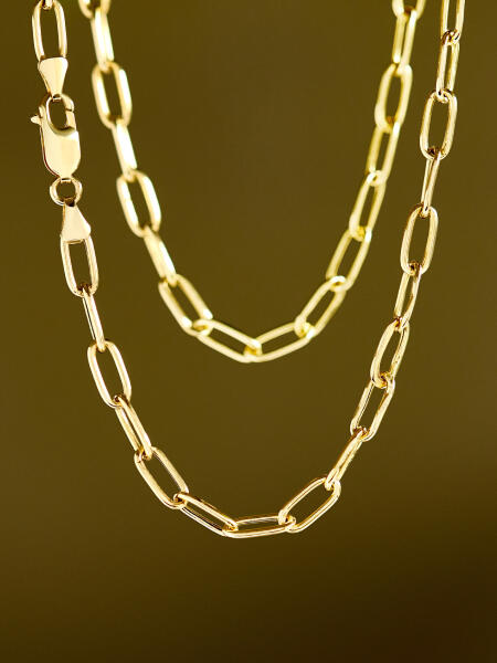 Two strands of a bold yellow gold chain shine against a blurred gradient background.