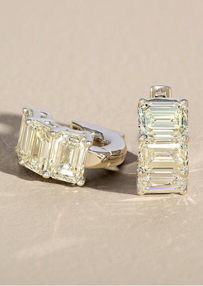 Emerald cut diamond earrings in white gold rest on a smooth tan surface. 