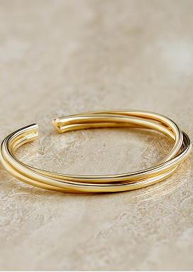 A yellow gold bangle with a twisted design reflects its glow on a smooth marble surface