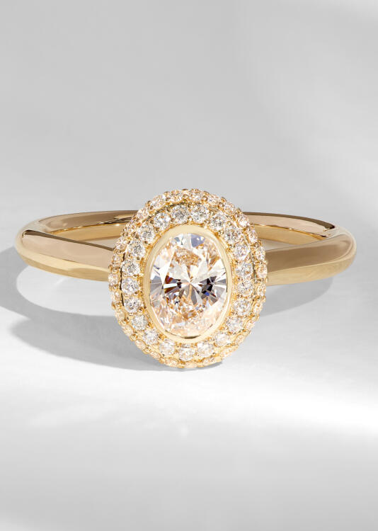 An oval diamond engagement ring in yellow gold with a double halo of round diamonds.