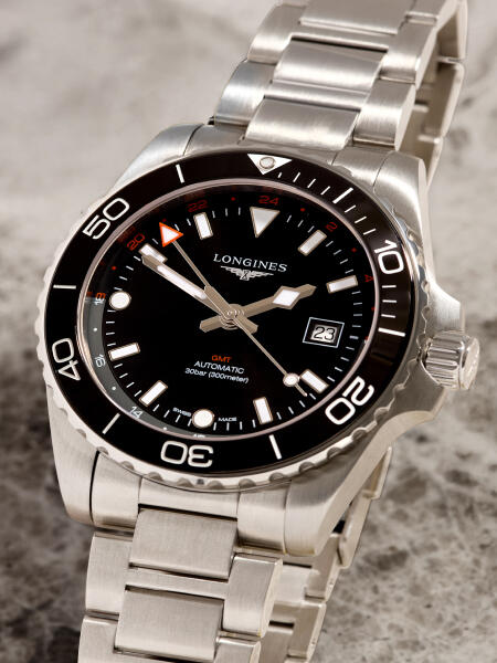 Dive watch with a black dial and stainless steel case and bracelet rests on a marble surface.